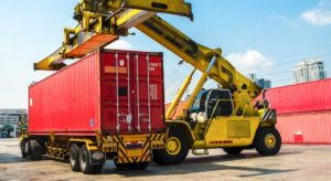 A construction vehicle loading a shipping freight container on to an 18 wheel truck flat bed.