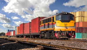 A train carrying shipping containers in a train yard filled with shipping containers.