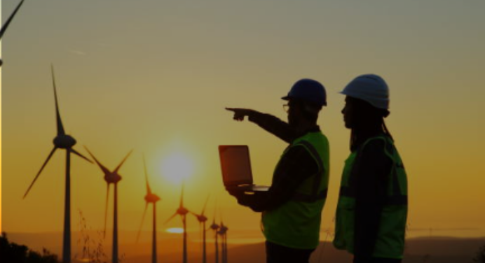 Two workers standing next to each other, one is holding a computer and pointing to wind turbines illustrating the word energy.