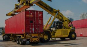 A construction vehicle loading a shipping freight container on to an 18 wheel truck flat bed.