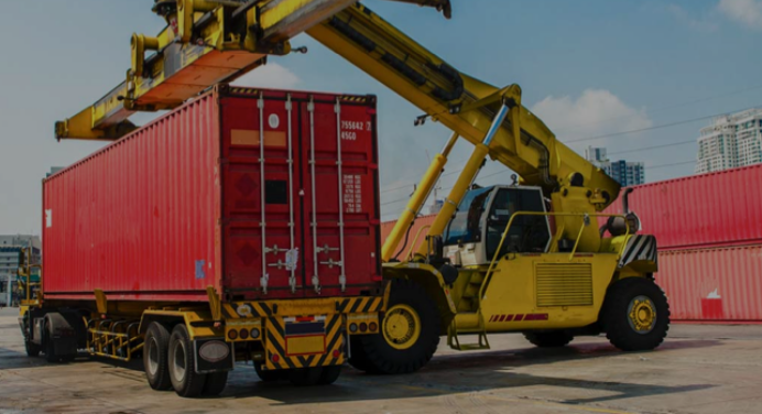 A construction vehicle loading a freight container on to an 18 wheel truck illustrating the words intermodal freight.