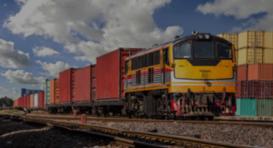 A train carrying shipping containers in a train yard filled with shipping containers.